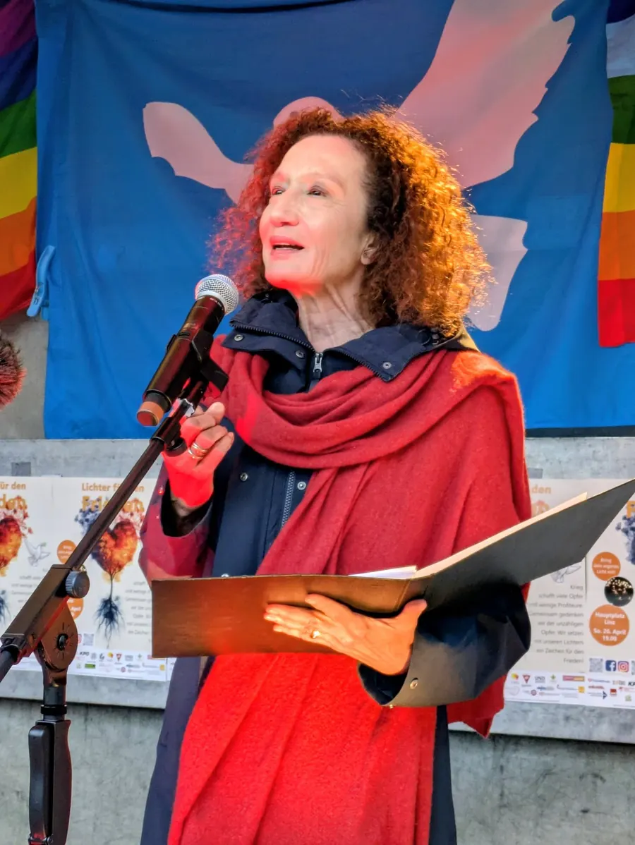 Eine Frau mit rotem Schal liest am Mikrofon aus einer Mappe vor