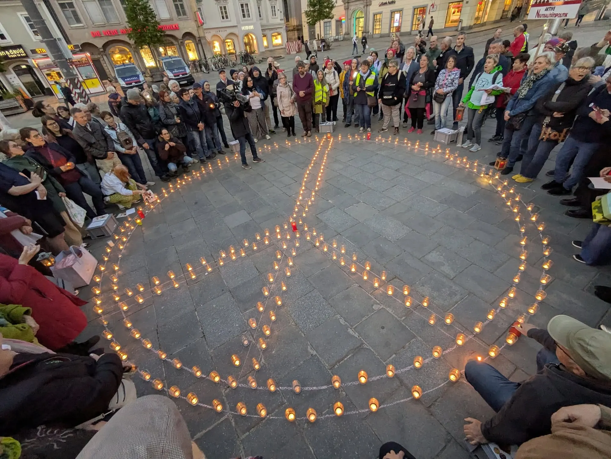 Von oben gesehen: ein großes Peace-Zeichen aus brennenden Kerzen auf dem Pflaster des Hauptplatzes, ringsum stehen dicht die Menschen