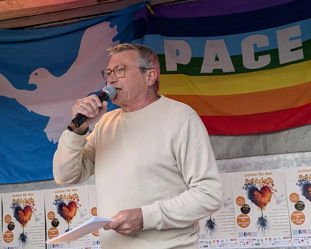 Ein Redner am Mikrofon vor der Pace-Fahne